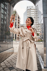 Woman waving to somebody with lovely smile during video call outside at the autumn street