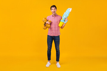 Fototapeta na wymiar Full size photo of young man happy positive smile hold water gun teddy bear toy play isolated over yellow color background