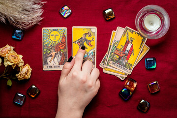 Fortuneteller's hand with black manicure lays out tarot cards, crystal, candle, dry roses on red...