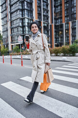 Calm multiracial woman walking with a paper cup of coffee and holding shopping bags