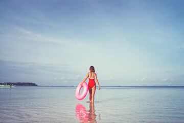 Enjoying suntan and vacation. Young woman in red swimsuit with pink rubber ring on the beach.