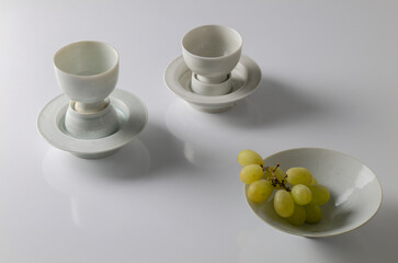 Still life of Chinese antique white porcelain cups and bowl with branch of white grapes on white table