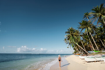 Fototapeta na wymiar Vacation on the seashore. Back view of young woman walking away on the beautiful tropical white sand beach.