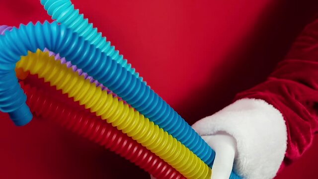 Group of multicolored rainbow toy pop it tube in Santas hand as flower on beige background, trend toy for the development of fine motor skills of hands, anti stress crackling tube.