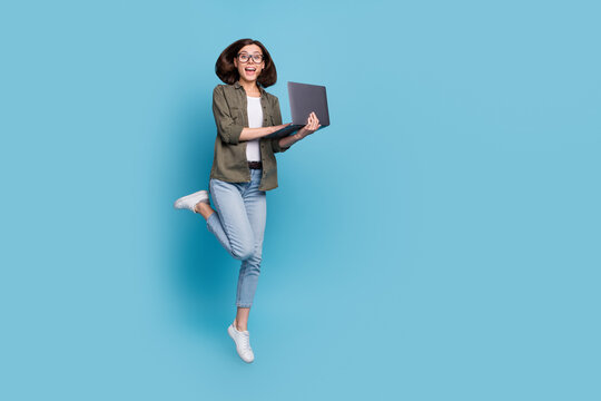 Full length photo of excited lady computer geek it developer jump use gadget wear shirt denim jeans isolated over blue color background