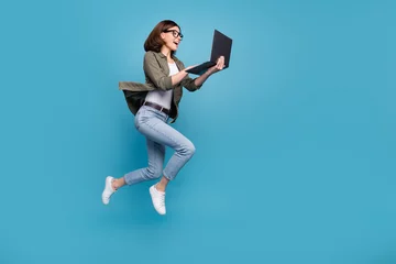 Tuinposter Profile side full size photo of excited lady ceo jump chatting netbook ap wear denim isolated over blue color background © deagreez