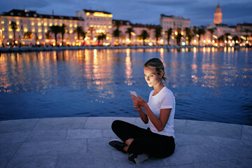 Fototapeta na wymiar Young woman using smartphone at city evening lights.