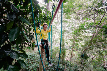 Young woman with climbing gear in an adventure extreme park climbing or passing on the rope road.