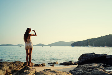 Fototapeta premium Young woman with long hear standing on sea beach enjoying the view.