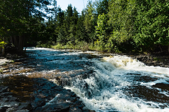 Waterfall in the Park; full view of rushing water after months of rain in Ocqueoc Falls in Northern Michigan with green trees framing the river