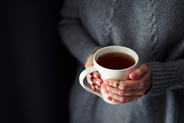 Cozy home. Female hands holding hot cup of coffee or tea.