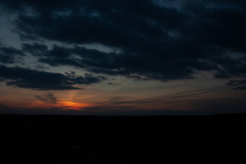 Naklejka na ściany i meble The red sun set below the horizon. Beautiful sunset and cloudy sky. 