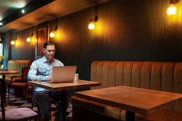 Freelance concept. Handsome young man working on laptop computer while sitting at cafe.