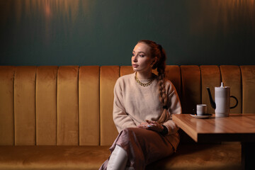 Drinking coffee. Pretty young woman holding cup of beverage while sitting at cafe.