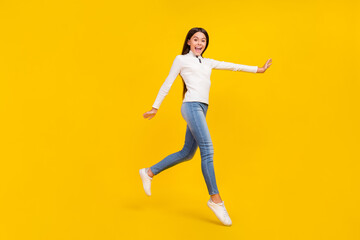 Full length photo of impressed brunette little girl run wear white pullover jeans sneakers isolated on yellow color background