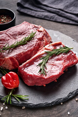 Two raw steak New York  with rosemary and spices on a piece of parchment paper on old dark stone background. Top view. Mock up.