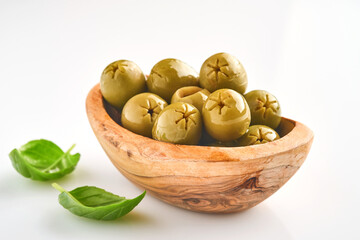 Delicious green olives with rosemary leaves in wooden bowl, isolated on white background.