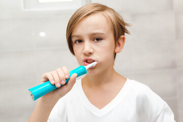 Kid brushing teeth with electic brush in bathroom. Dental hygiene every day. Health care, childhood...
