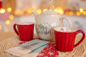 White Ceramic TeaPot with text Merry Christmas and cups with marshmallows on xmas bokeh background