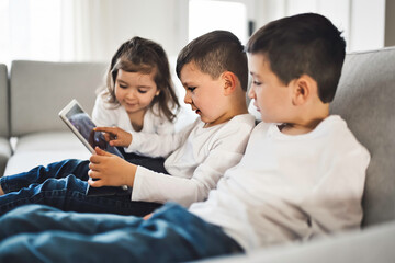 Childs relaxing with their tablets on a comfortable sofa at home