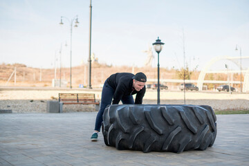 active sportsman lifting and pushing huge tire, doing workout outdoors