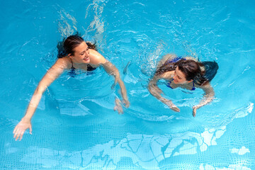 Two happy attractive brunette female friends in bikini stands in hotel indoor swimming pool. Above view.