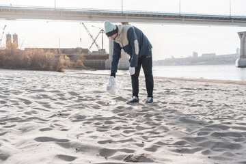 young male volunteer collecting plastic garbage trash on the sandy beach, protecting environment