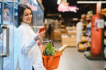 Smiling young woman using mobile phone while shopping in shopping store