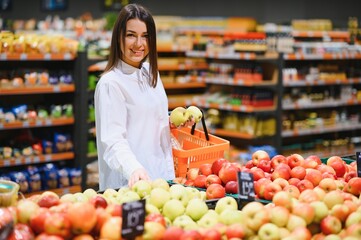 woman in a supermarket at the vegetable shelf shopping for groceries, she is choosing