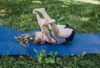 a little girl does yoga lying on a sports mat in the park