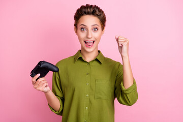 Photo of impressed lucky young woman dressed green shirt holding playstation rising fist smiling isolated pink color background © deagreez