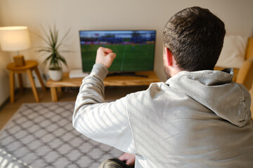 Man on the couch is watching TV. Football fan watches football and rejoices at the victory. Entertainment and sports concept. Watching sports, movies on TV at home