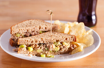 Tuna salad sandwich on wheat bread with potato chips and soda; copy space