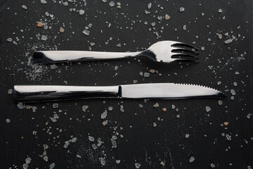 Black stone board with cutlery and sea salt. Top view.