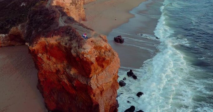 Aerial of woman doing yoga on a rocky cliff edge over beach in Santa Cruz