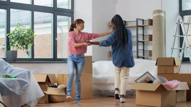 moving, people and real estate concept - women with boxes dancing at new home