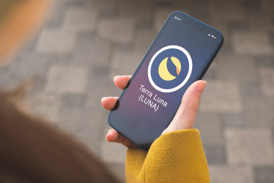 Terra Luna cryptocurrency symbol, logo. Business and financial concept. Hand with smartphone, screen with crypto icon close-up