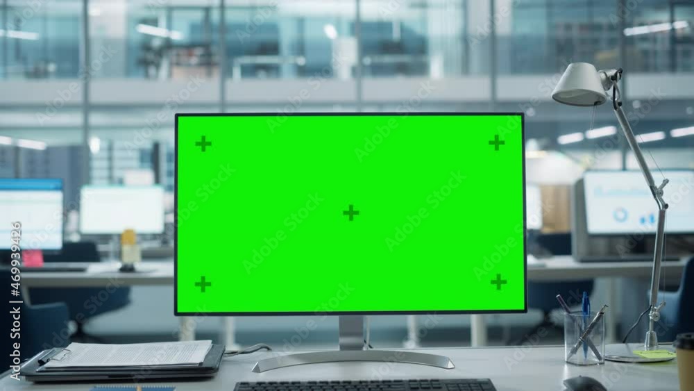 Poster Desktop Computer Monitor with Mock Up Green Screen Chroma Key Display Standing on the Desk in the Modern Business Office. In the Background Glass Wall with Big City Office. Zoom in Shot.