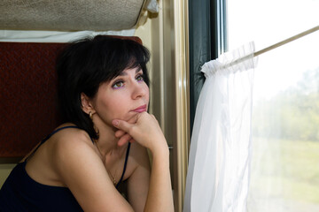A pensive beautiful woman is sitting at the window on the train remembering her vacation.
