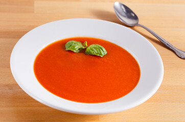 Fresh homemade tomato soup in a white bowl with basil garnish; copy space