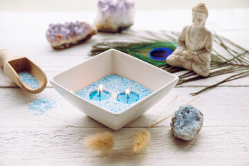 Blue and white granulated wax crystals to create candles by pouring in bowl and inserting wick. Handmade sand candle in white ceramic bowl on white wooden background, crystal geodes for decoration.