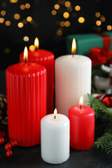 Fototapeta na wymiar Burning candles and festive decor on dark table against blurred Christmas lights