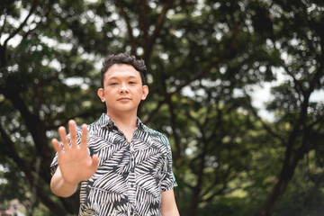 A young asian man refuses to cooperate, extending his hand out to make a stop gesture while looking...