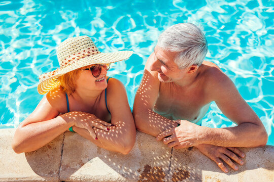 Senior couple relaxing in swimming pool. People enjoying summer vacation in hotel. All inclusive.
