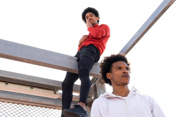Black male sitting on beam above ethnic man on street