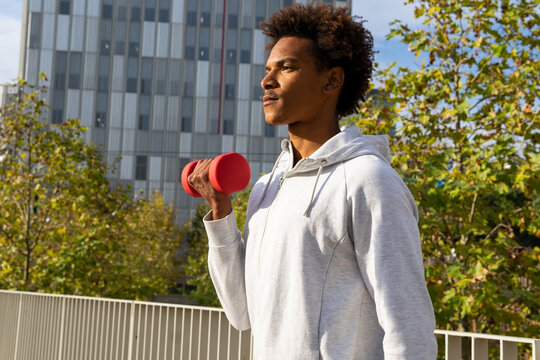 Ethnic guy doing dumbbell exercise on summer street