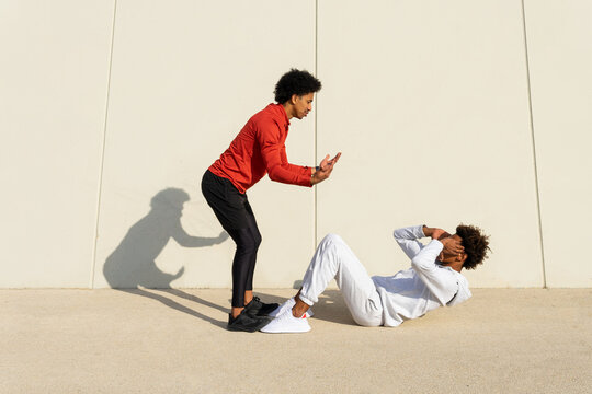 Ethnic trainer instructing black guy performing abs exercises on street