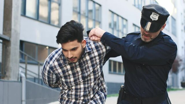 Waist up portrait view of the cop handcuffing caucasian young man and going with him to the patrol car. Criminal concept
