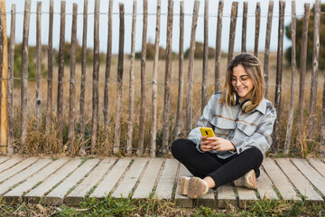 Young female millennial resting on stone border while using mobile phone at roadside