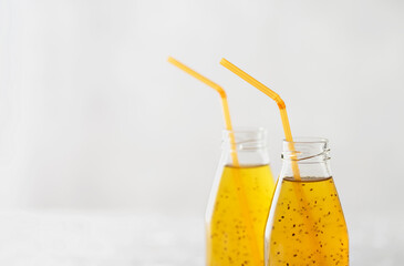 Passion fruit drink with chia seeds in glass bottles with tubes. Grey background